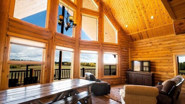 A log cabin with large windows, a dining table, a sofa, and a fireplace. - Warm River Butte Lodge (Ashton)