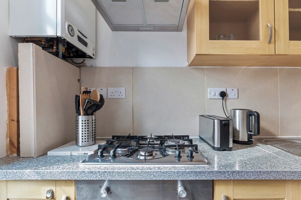 A kitchen with a gas stove, a toaster, and a kettle. There are cabinets above the stove and a countertop with a sink.