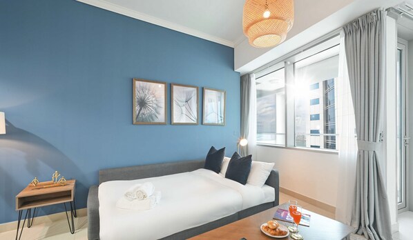 Een moderne hotelkamer met een blauwe accentmuur, een groot bed, een tafeltje met ontbijt en uitzicht op de stad door het raam.