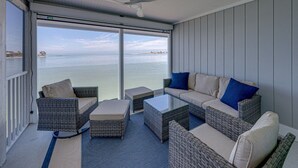 Ein Balkon mit Korbmöbeln, einem Deckenventilator und Blick aufs Meer.