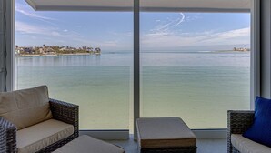 Ein Balkon mit Blick auf ein ruhiges Meer und eine entfernte Küste, ausgestattet mit Korbstühlen und einem kleinen Tisch.