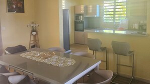 A dining area with a glass table, four chairs, a vase with flowers, and a wooden ceiling. - House between mountains and sea. (Deshaies)