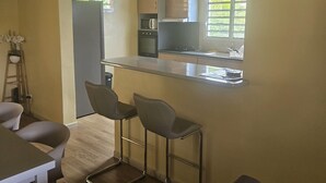 A compact kitchen with a central island, a dining area with two chairs, and a small table. - House between mountains and sea. (Deshaies)