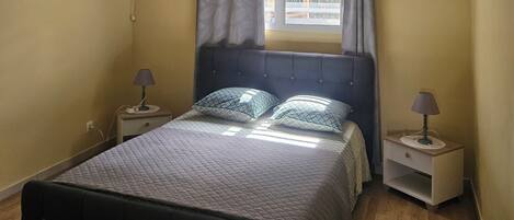 Un dormitorio con cama, mesitas de noche, una ventana con cortinas, un equipo de aire acondicionado y techo de madera.