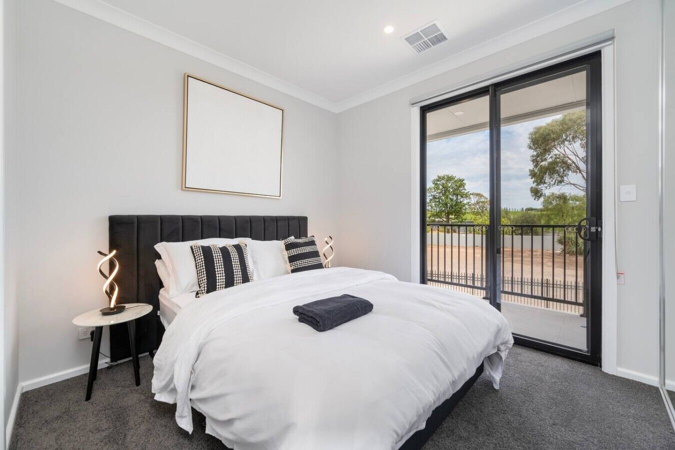 A bedroom with a large bed, a nightstand, a framed picture, and a sliding glass door leading to an outdoor area.