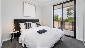 Ein Schlafzimmer mit einem großen Bett, einem Nachttisch, einem gerahmten Bild und einer Schiebetür zu einem Außenbereich.