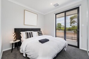 Un dormitorio con una cama grande, una mesita de noche, un cuadro enmarcado y una puerta corrediza de vidrio que da a un espacio exterior.