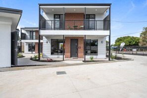A modern two-story building with a flat roof, a brick facade, and a balcony with metal railings.