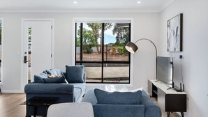 Ein modernes Wohnzimmer mit einer Couch, einem Couchtisch, einem Fernseher und einem großen Fenster mit Blick ins Freie.