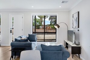Una sala de estar moderna con un sofá, una mesa de centro, un televisor y un ventanal con vistas al exterior.