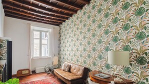 Ein gemütlicher Raum mit gemustertem Tapeten, einem braunen Ledersofa, einem roten Teppich mit Muster und einer Holzzieldecke.