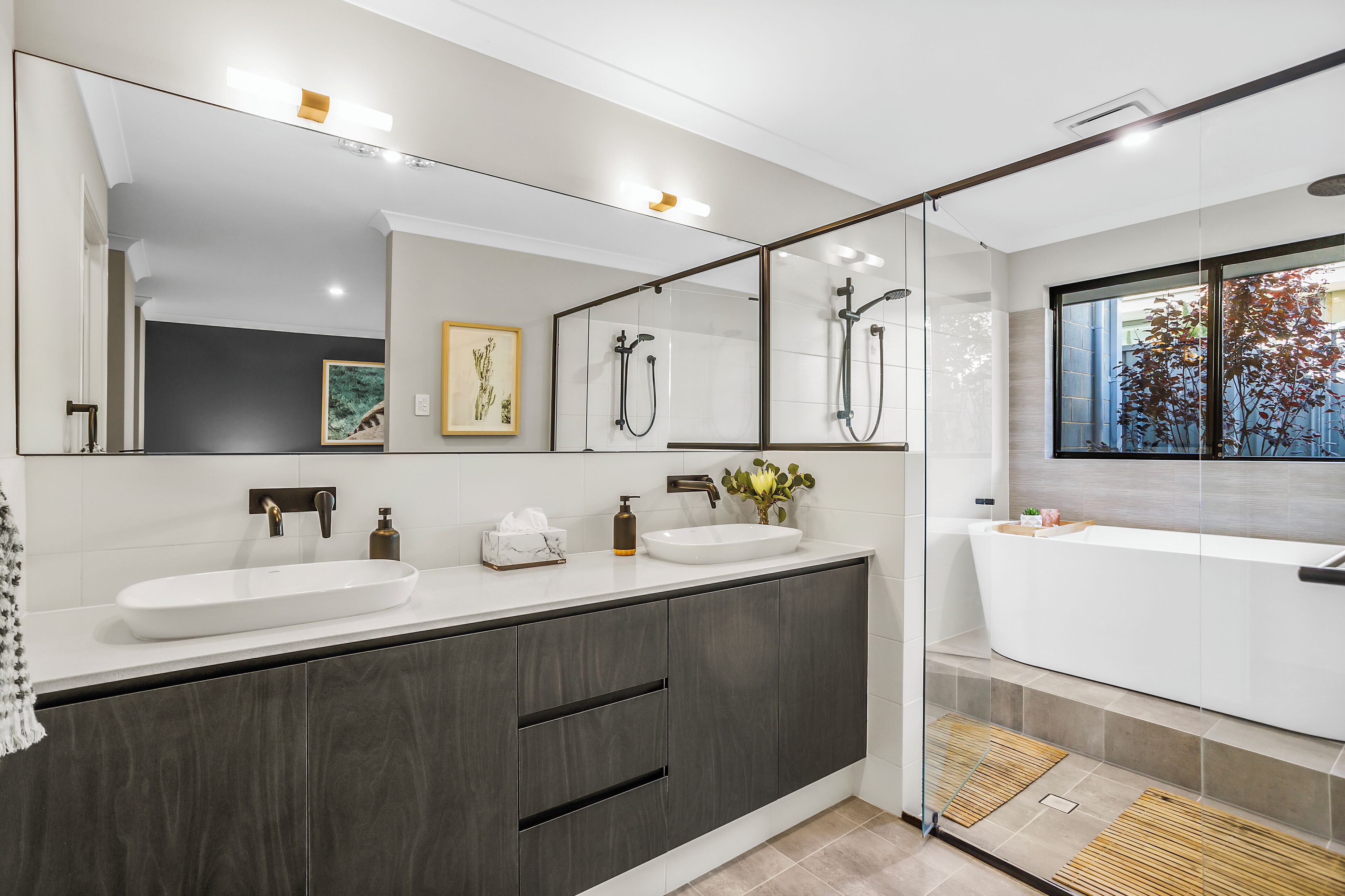 A modern bathroom with a large mirror, dual sinks, a bathtub, and a shower.