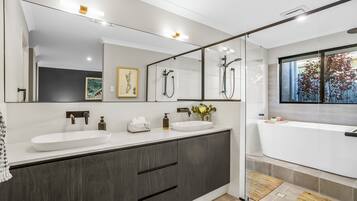 A modern bathroom with a large mirror, dual sinks, a bathtub, and a shower.
