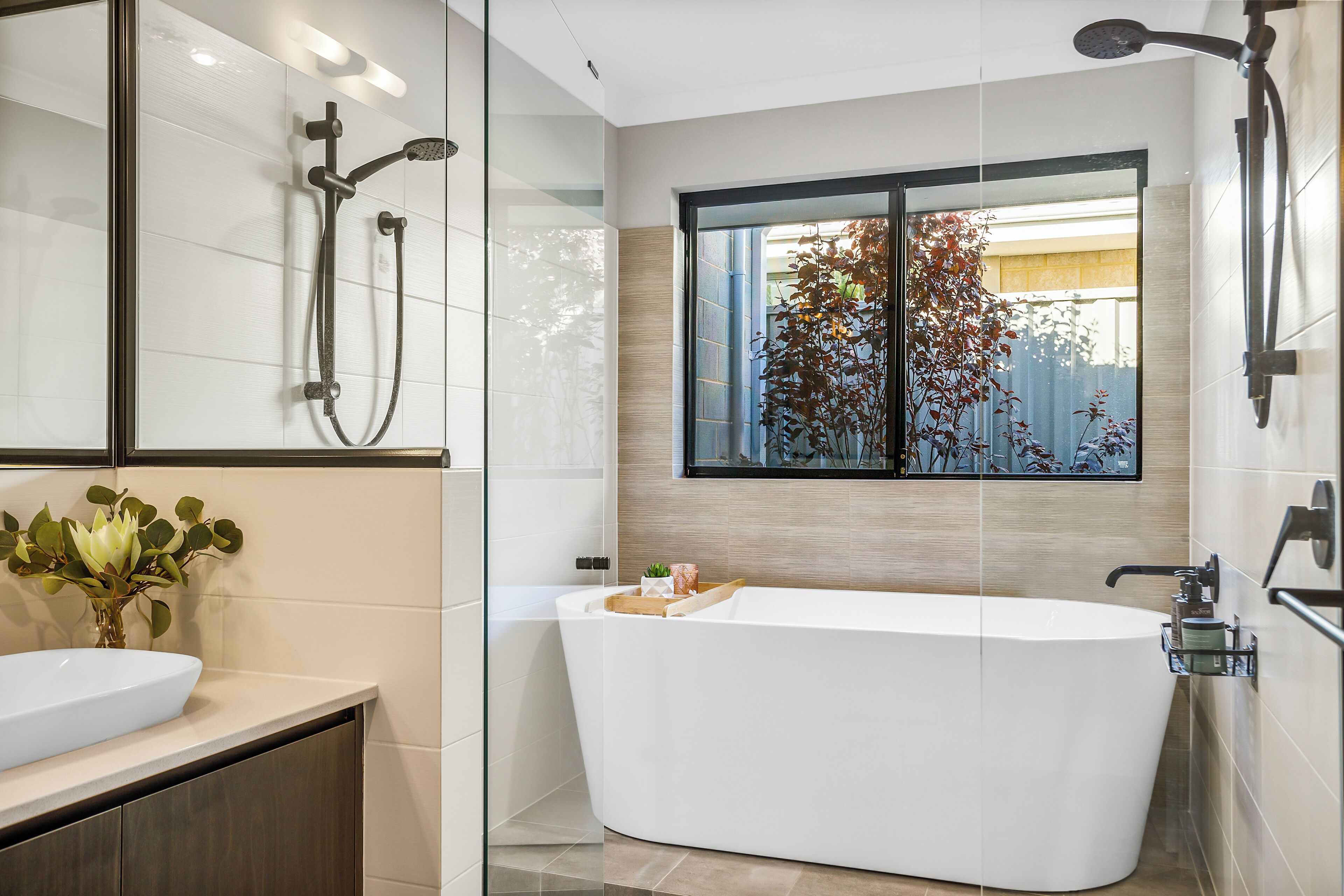 A modern bathroom with a freestanding bathtub, a glass shower enclosure, a large mirror, and a window with a view of trees.