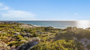 A coastal landscape with a beach, vegetation, and a building with a blue roof.