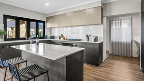 A modern kitchen with a large island, dark cabinetry, and a view of the outside.