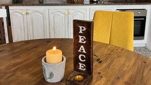 Una mesa de comedor con una vela y un letrero de madera que dice "PEACE".
