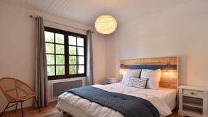 A bedroom with a bed, a nightstand, a chair, a window, and a hanging light fixture. - House with swimming pool 300 metres from the beach and center (La Couarde-sur-Mer)