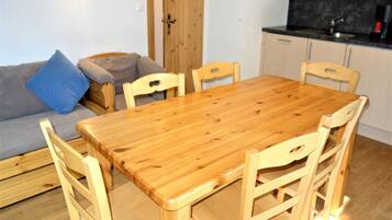 Ein kompakter Wohnbereich mit einem Holzespeisetisch, umgeben von Stühlen, einer Couch mit Kissen und einer Küchenzeile mit Schränken und Arbeitsplatte.