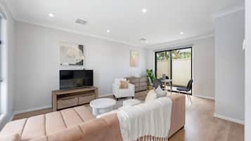 A modern living room with a large sofa, a flat-screen TV, and a dining area with chairs and a table.