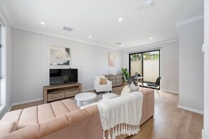 A modern living room with a large sofa, a flat-screen TV, and a dining area with chairs and a table.