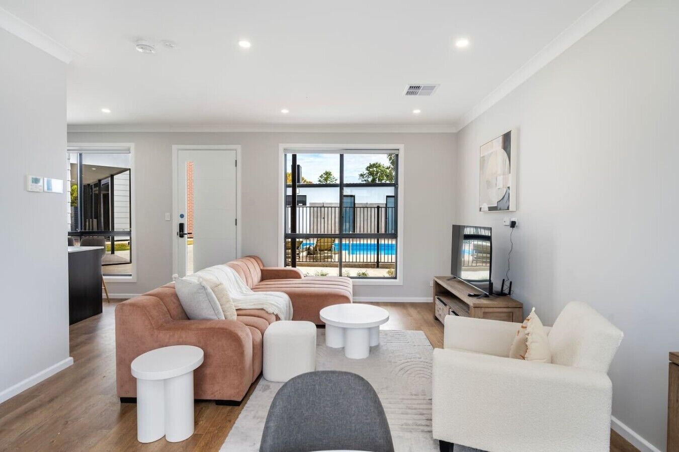 A modern living room with a sofa set, a coffee table, and a TV. There is a balcony with a view of the sea.