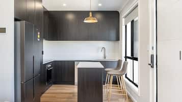 A modern kitchen with dark cabinetry, a stainless steel refrigerator, a central island with stools, and a pendant light.