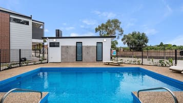 A swimming pool with a small building in the background, surrounded by a fence.
