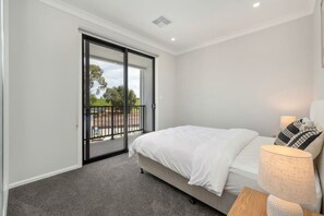 A bedroom with a bed, a nightstand, a lamp, and a sliding glass door leading to a balcony.