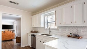 Una cocina moderna con armarios blancos, encimera de mármol y lavavajillas.