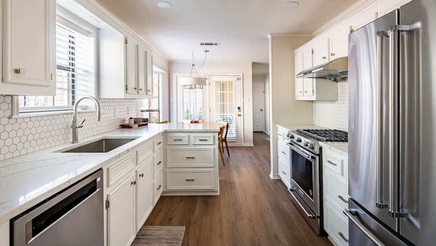Una cocina con muebles blancos, un refrigerador de acero inoxidable y un horno empotrado.