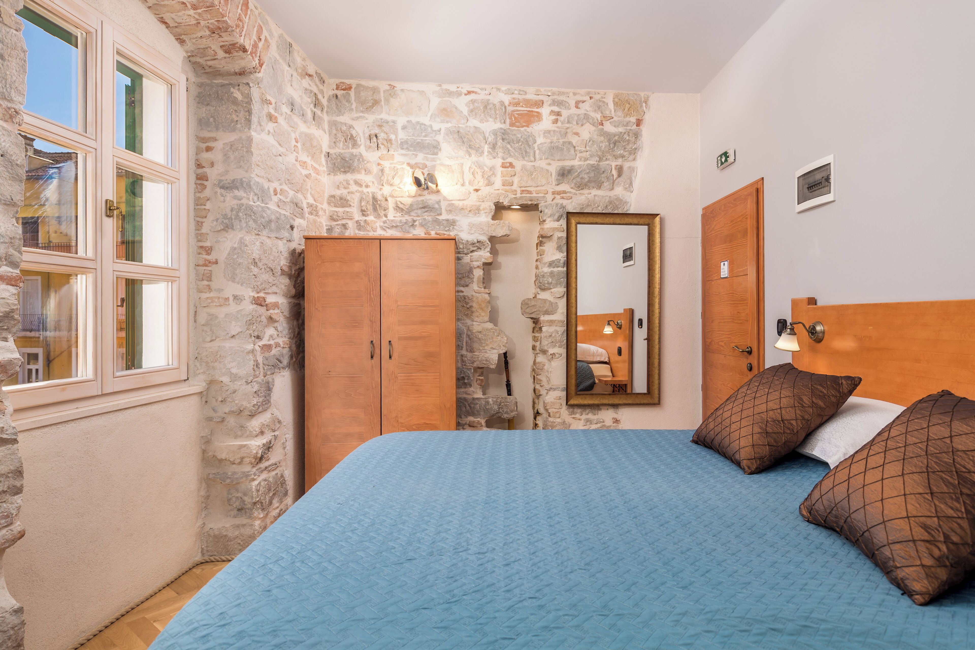Une chambre avec un mur en pierre, une armoire en bois et un lit avec une literie bleue.