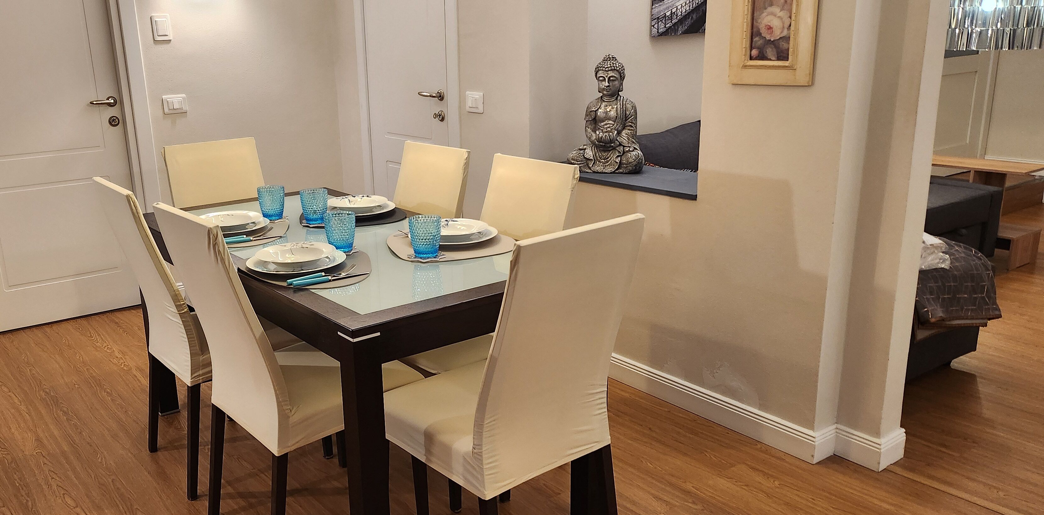 Un comedor con una mesa dispuesta para cuatro, sillas y una estatua de Buda en un estante.