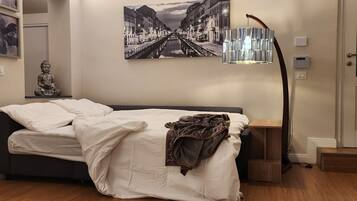 Een slaapkamer met een Galaxy Z Flip4 bed, een Boeddhabeeld, een ingelijst stadsgezicht en een moderne vloerlamp.