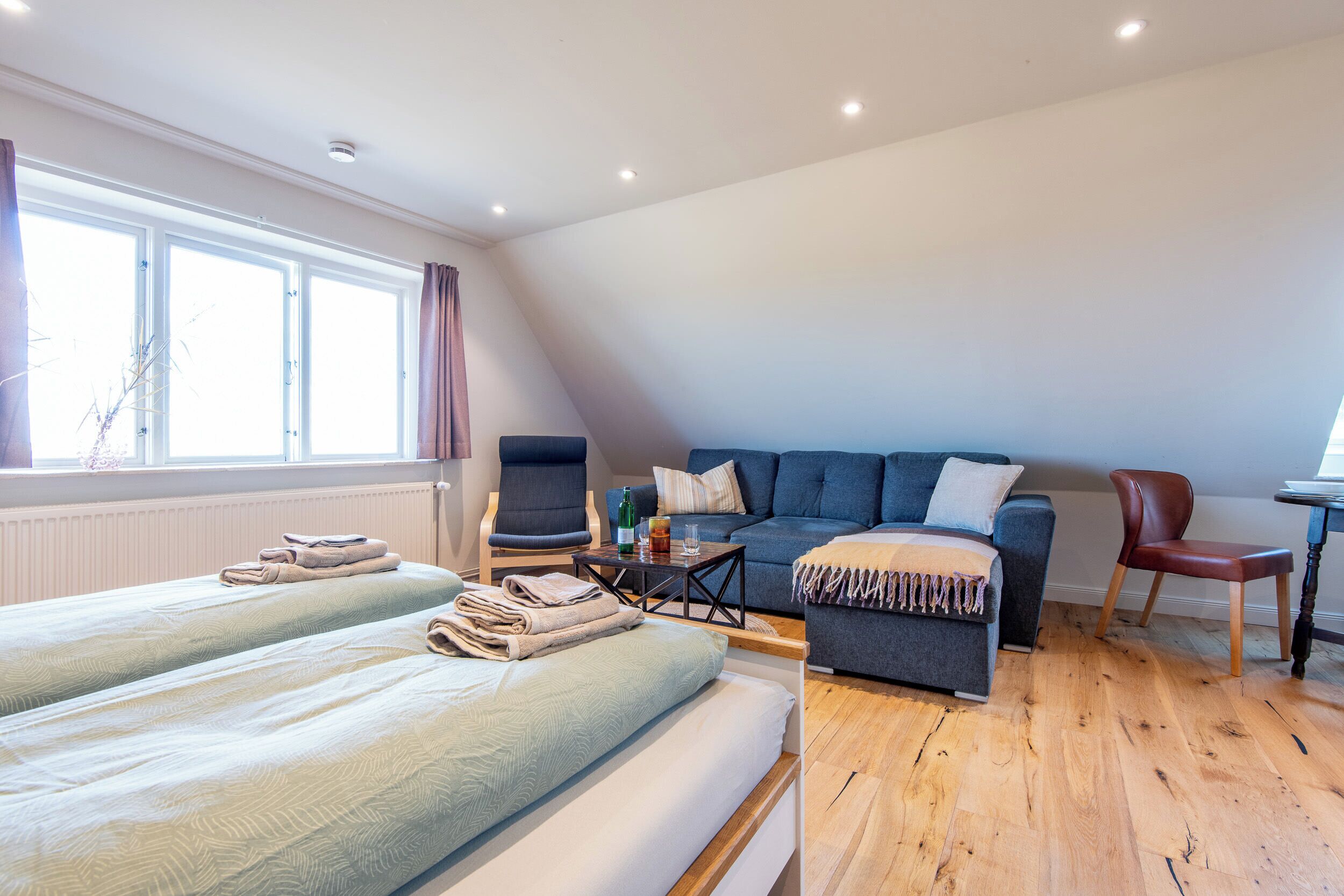 Een kamer met twee bedden, een bank, een stoel, een kleine tafel en een raam met gordijnen.