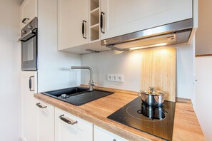 A modern kitchen with white cabinets, a black sink, a stainless steel range hood, and a built-in induction cooktop. - Sandpiper on the Wadden Sea in the German-Danish meadows, pet friendly! (Rodenäs)