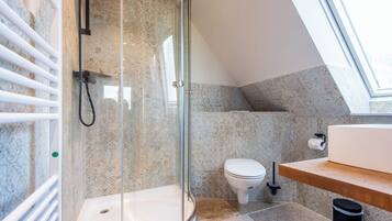 Et moderne badeværelse med en brusekabine i glas, toilet og en vask med træbordplade.