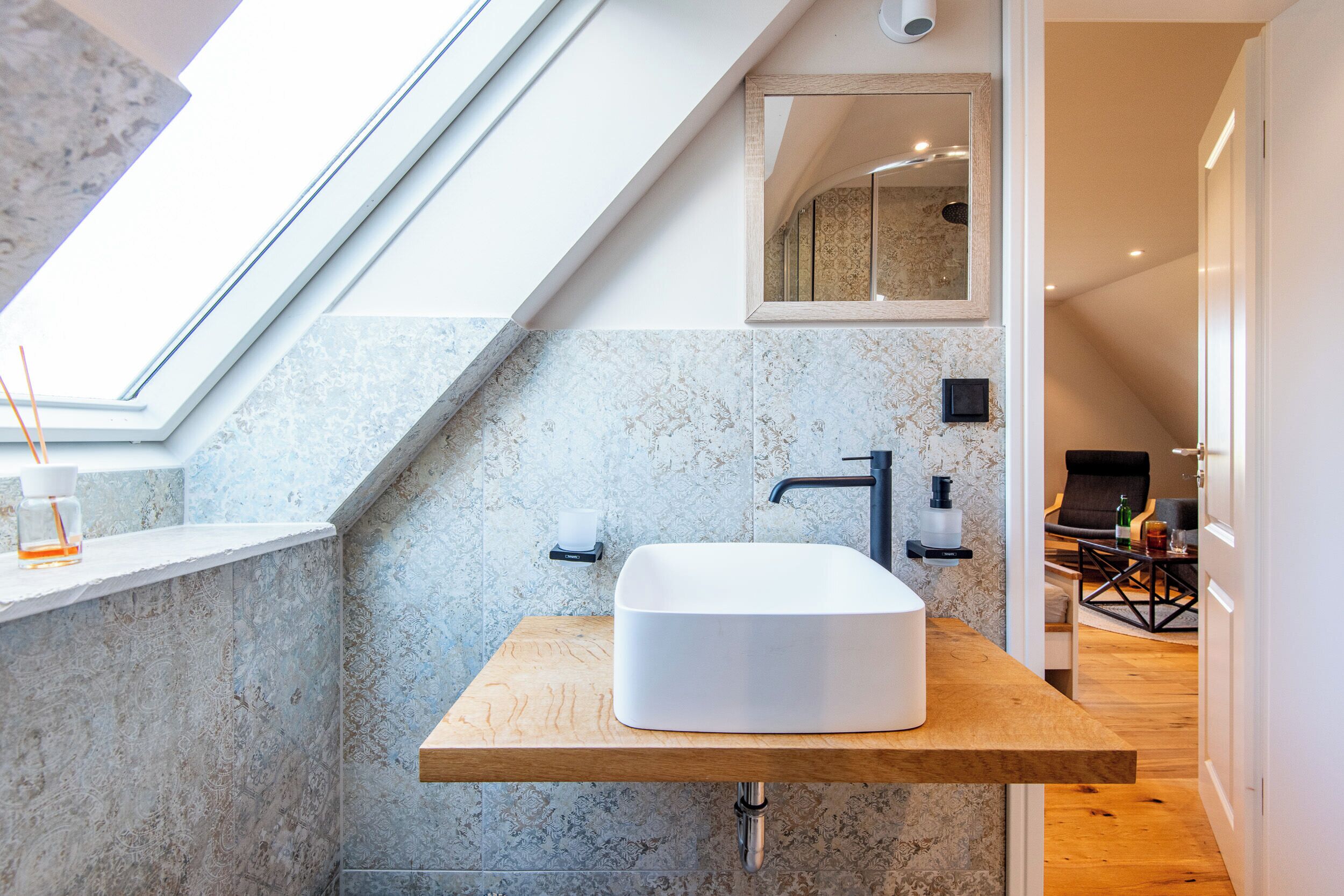 Een moderne badkamer met dakraam, een grote spiegel en een houten wastafelmeubel.