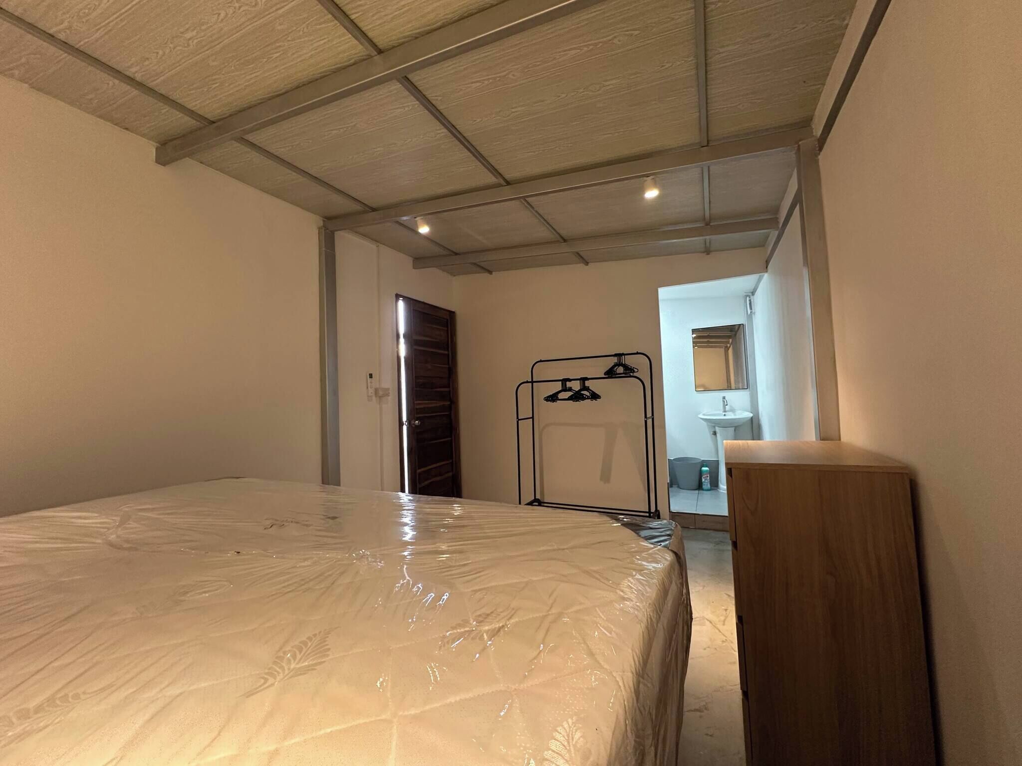 Un dormitorio con cama, un armario de madera, una puerta y un pasillo que da a un baño.