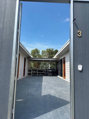 Puerta abierta que da a un espacio exterior cubierto con un patio, mesas y sillas.