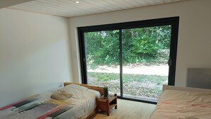 Un dormitorio con dos camas, una ventana con vistas a zonas verdes y una mesita de noche con lámpara.
