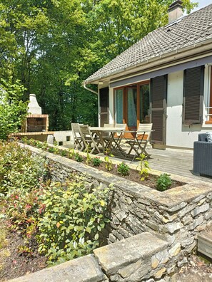Una casa con un muro de piedra, un patio con muebles de exterior y un jardín con diversas plantas.