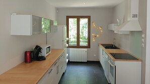 Cocina compacta con encimera de madera, microondas integrado, hervidor y ventana con vistas a zonas verdes.