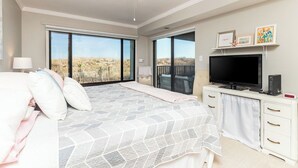 Un dormitorio con una cama grande, televisión y balcón con vista a la playa.