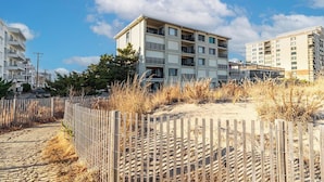 Un edificio de varios pisos con balcones, ubicado cerca de una zona arenosa con valla de madera.