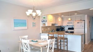 Una cocina moderna con armarios blancos, una isla central y un comedor con sillas blancas.