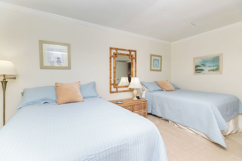 A hotel room with two beds, a nightstand, a lamp, and framed artwork on the walls.