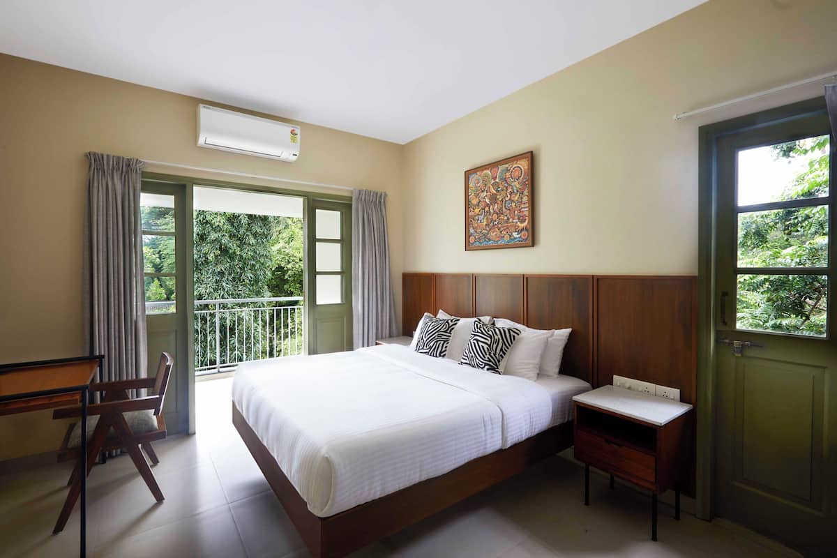 Ein Schlafzimmer mit einem großen Bett, einem Schreibtisch und einem Stuhl. Ein Fenster mit Vorhängen, ein Bild an der Wand und eine Tür sind ebenfalls vorhanden.
