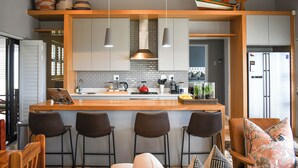 Een moderne keuken met een centraal eiland, barstoelen, hanglampen en een zichtbare koelkast.