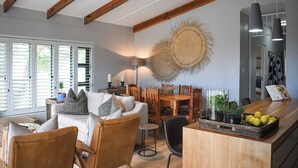 Een moderne woonkamer met een bank, stoelen, een eettafel en een keukenhoek met een fruitmand.